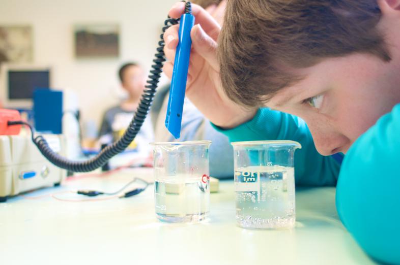 Ein junger Schüler füllt eine Flüssigkeit mit einer Pipette in einen Behälter. Szene aus dem Chemieunterricht.